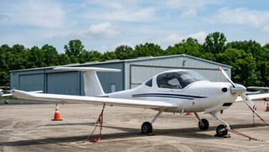 A white low-wing single-engine training airplane parked on a general-aviation ramp under a summer sky