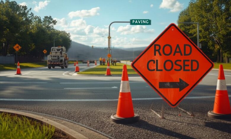Orange ROAD CLOSED detour sign and traffic cones at a Murfreesboro parkway intersection with a paving crew at work