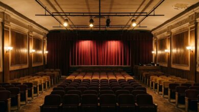 Warmly lit historic community theatre auditorium with red velvet stage curtains and rows of empty seats (illustrative)