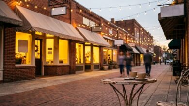 Brick storefronts with glowing windows at dusk, with two coffee cups on a cafe table in the foreground.