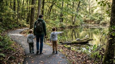 A parent and two children, seen from behind on a wooded path, as one child points at a turtle on a log by a pond.